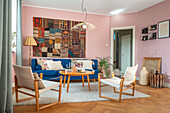 Living room with tapestry, blue sofa, pink walls and wooden furniture on carpet