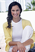 Dunkelhaarige Frau in weißem Top, gelber Strickjacke und weißer Hose