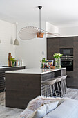 Kitchen island with bar stools and modern pendant light in open-plan living room