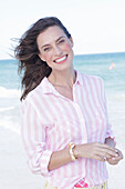Brunette woman in pink striped blouse on the beach