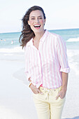 Brünette Frau in rosa gestreifter Bluse und heller Hose am Strand