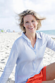 Blonde Frau in hellblau gestreiftem Hemd und orangefarbenen Shorts am Strand