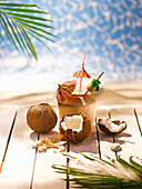 Coconut, one broken, one whole, and a wooden cocktail cup against a tropical backdrop