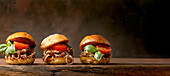 Homemade mini burgers with stew beef, tomatoes and basil on wooden background