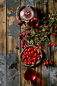 Rose hip berries herbal tea in glass teapot and cup on old wooden plank background with wild autumn berries around