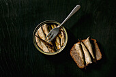 Open can with canned baltic smoked sprats sardine in oil with slice of rye bread and fork