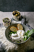 Traditional italian burrata knotted cheese salad in grey ceramic bowl on table, sliced bread, olives, green sprouts around