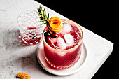 Cranberry orange margarita on the edge of a counter with an orange peel rose and sprig of rosemary