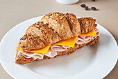 Delicious croissant with ham and cheese placed on white plate