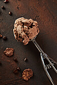 Detail of a scoop of chocolate ice cream scooped up with a ladle on a rustic brown background