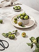 Green fresh plums arranged with tableware on table covered with tablecloth
