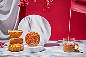Milk pouring into glass with hot drink on table with sweet Chinese mooncakes on red background