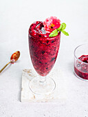 Glass with sweet berry smoothie garnished with flower served on white background