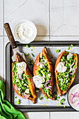 Baked sweet potatoes with mashed green pea and parsley gremolata, crumbled feta, red onion and sour cream sauce