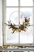 DIY wreath with dried flowers on an old window with a view of a snowy landscape