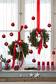 Festively decorated window with red Christmas baubles, wreaths, candles and fir branches