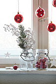 Christmas window decoration with red baubles, fir branch and storage jars