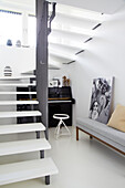 Piano and grey upholstered bench in alcove under stairs