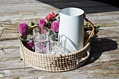 Woven tray with pitcher, glasses and dahlias on a wooden background