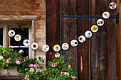 DIY garland made from round plates with flowers on wooden wall in outdoor area