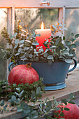 Vintage enamel bowl with eucalyptus and burning candle, in front pomegranate