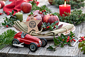 Weihnachtsgedeck mit Äpfeln, Ilexzweigen 'Blue Princess' und Spielzeugauto