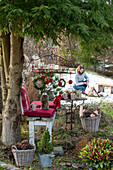 Weihnachtsplatz im Garten - mit Kissen, Hängetablett,  Windlichtern und mit Juteschnur umwickelte Christbaumkugeln, Frau im Hintergrund