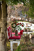 Weihnachtsplatz im Garten - mit Kissen, Hängetablett Hängetablett mit Windlichtern und mit Juteschnur umwickelte Christbaumkugeln, im Vordergrund Hocker mit Kissen und Thermosflasche