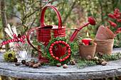 Christmas arrangement with red watering can, pine branches, ornamental apples, and clay pots