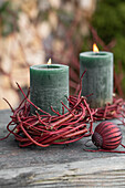 Brennende Kerze mit Kränzchen aus rotem Hartriegel (Cornus sanguinea) und Christbaumkugel