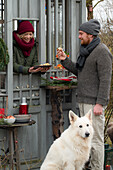 Woman handing Christmas cookies through the window, man with dog in the foreground