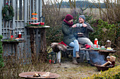 Mann und Frau mit Glühwein und Weihnachtsgebäck auf Bank sitzend im Garten