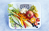 Slimming cure: Various fruits and vegetables on a bathroom scale