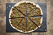 Pizza mit Blattgemüse, Pistazien, Pinienkerne und Granatapfel, geschnitten auf Schieferplatte