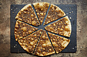 A pizza topped with cumin and sesame seeds, sliced on a slate platter