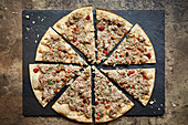 A pizza topped with pork sausage, pomegranate seeds and pine nuts, sliced on a slate platter