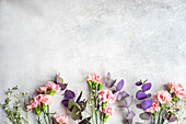 Zutaten für Frühlingsblumenstrauß mit rosa Nelken auf Betonuntergrund
