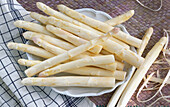White asparagus spears on a plate next to a checked tea towel