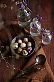 Vintage bowl with quail eggs and apothecary bottles with purple flowers on awooden table