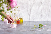 Salbentöpfchen mit Hand, Aromaöle im Flacon, sowie Kamillen- und Rosenblüten