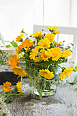 Bouquet of marigolds (Calendula officinalis), in a glass vase wrapped with clematis fruit stands