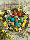 Colorful Easter eggs, sugar eggs, and quail eggs in a wreath with daffodils