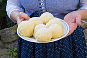 Woman in dirndl holds plate of raw potato dumplings 'half and half'