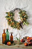 Adventskranz mit Orangenscheiben und Kerzen auf Holztisch, Äpfel daneben