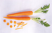 Peeled carrots with greens on a light background