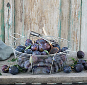 Plums in wire basket, with a wooden cooking spoon and whisk