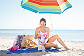 Junge blonde Frau im Badeanzug sitzt unter Sonnenschirm am Strand