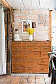 Wooden chest of drawers with decorative objects against rustic-style brick wall
