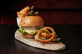 Cheese burger in brioche bun with onion rings, pickles and topped with cornichons