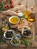 Stillleben mit Ciabatta, verschiedenen Sorten Olivenöl, Oliven, Salz, Tomaten, Basilikum